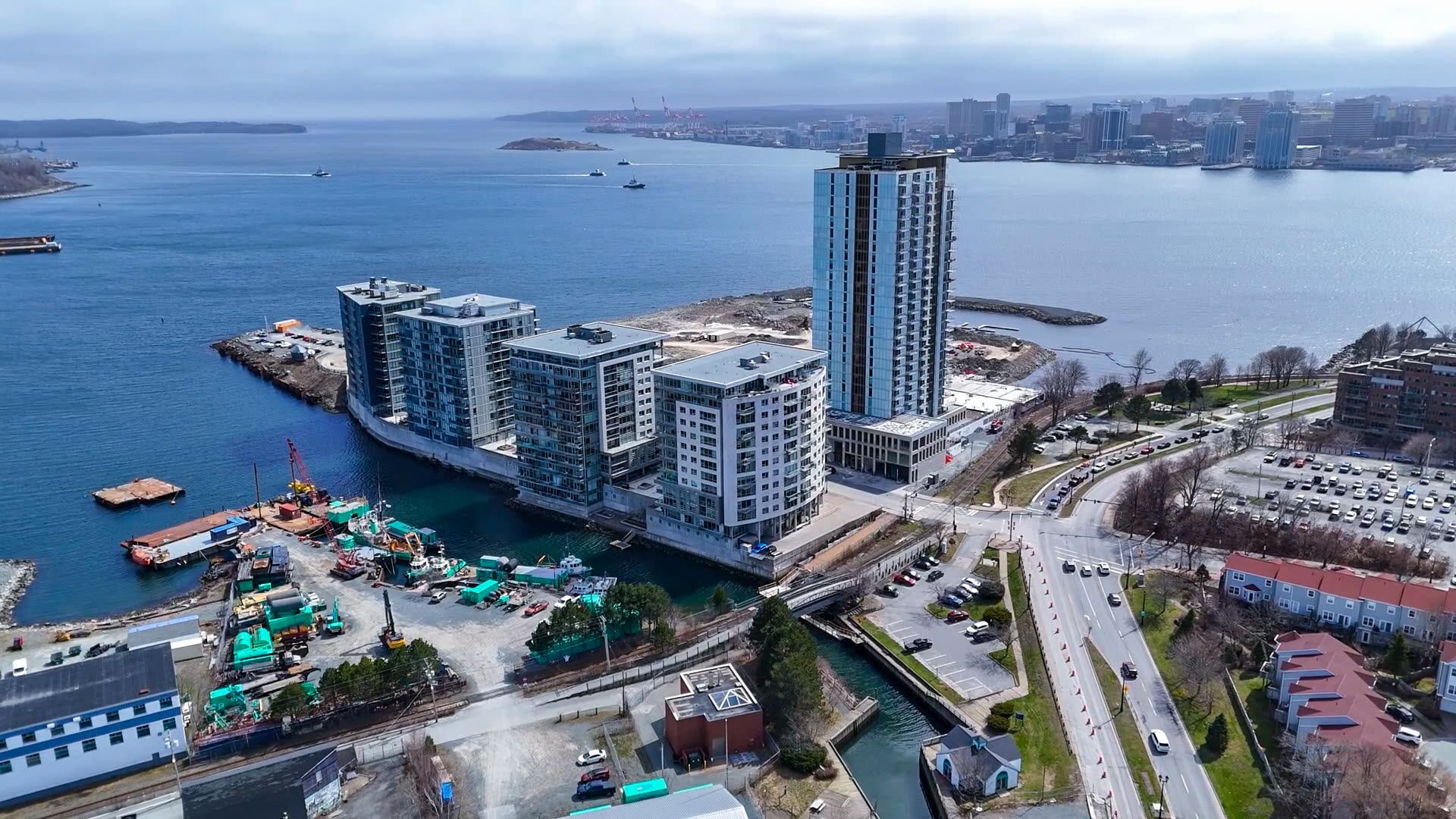 Aerial view of modern glass residential towers and mid-rise buildings on a harbour peninsula, with Halifax skyline across the water.